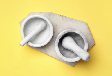 Photo of Ceramic mortars with pestles and marble board on yellow background, top view. Cooking utensils