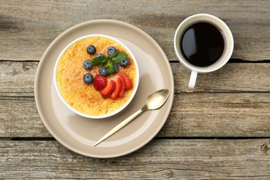 Photo of Delicious creme brulee with berries and mint in bowl and coffee on wooden table, flat lay
