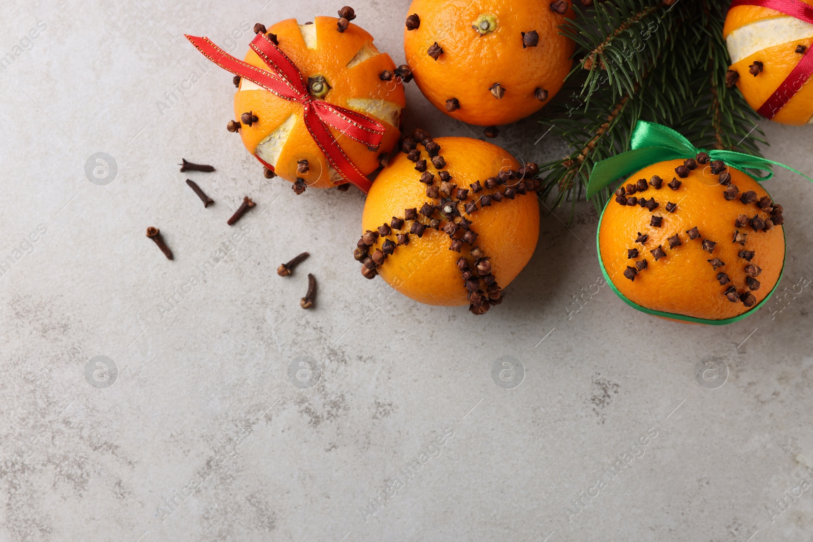 Photo of Pomander balls made of tangerines with cloves and fir branches on grey table, flat lay. Space for text