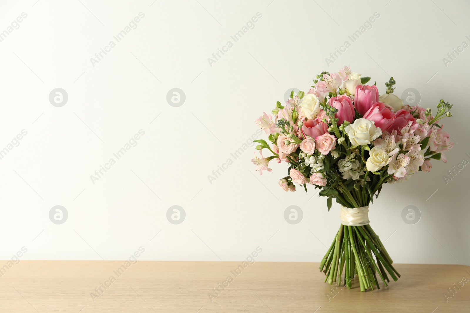 Photo of Beautiful bouquet of fresh flowers on wooden table near light wall. Space for text