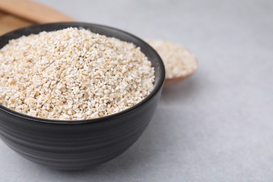 Photo of Dry barley groats in bowl on light grey table, closeup. Space for text