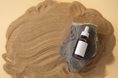 Photo of Bottle of serum and stone on sand against beige background, top view. Space for text