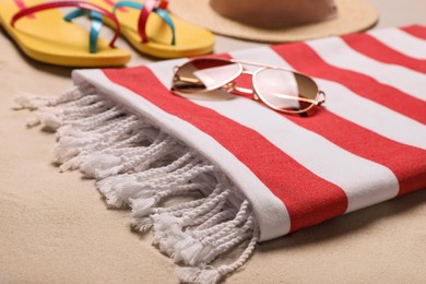 Photo of Beach towel, sunglasses, hat and flip flops on sand, closeup