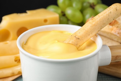 Photo of Pot of tasty cheese fondue and bread stick on table, closeup