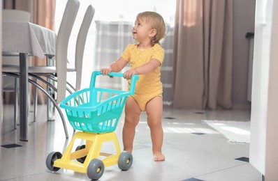 Photo of Cute baby with toy walker in room. Learning to walk