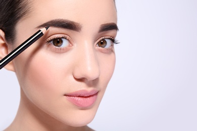 Photo of Beautiful woman with perfect eyebrows applying makeup on light background