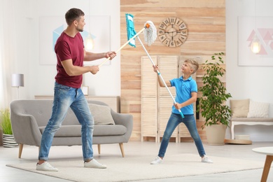 Photo of Dad and son having fun while cleaning living room together
