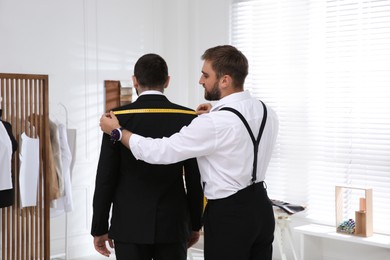Photo of Professional tailor measuring client's shoulder width in atelier