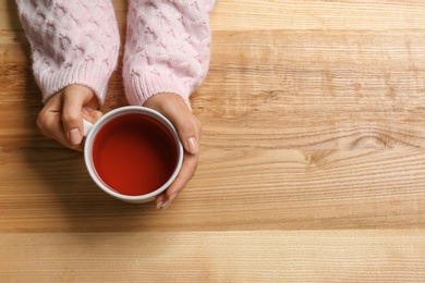 Woman holding cup of tea at wooden table, top view. Space for text