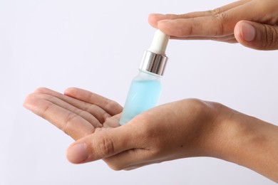 Photo of Woman with bottle of cosmetic serum on white background, closeup
