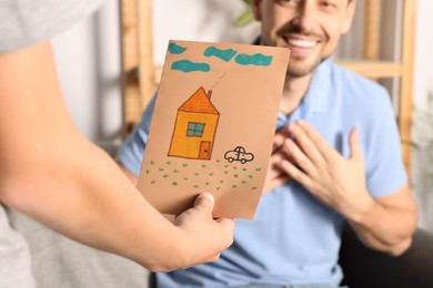 Photo of Happy man receiving greeting card from his son at home, closeup