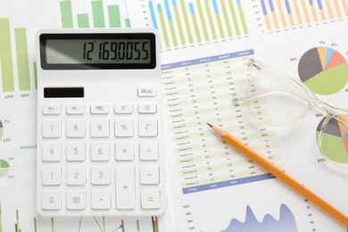 Photo of Calculator, pencil and glasses on accounting documents with graphs, flat lay