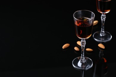 Photo of Liqueur glass with tasty amaretto and almonds on black table. Space for text