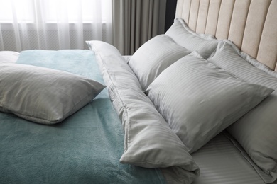 Photo of Comfortable bed with soft blanket and pillows indoors, closeup