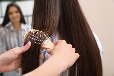 Photo of Woman combing friend's hair with cushion brush indoors, closeup