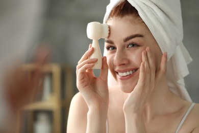 Photo of Washing face. Young woman with cleansing brush near mirror in bathroom