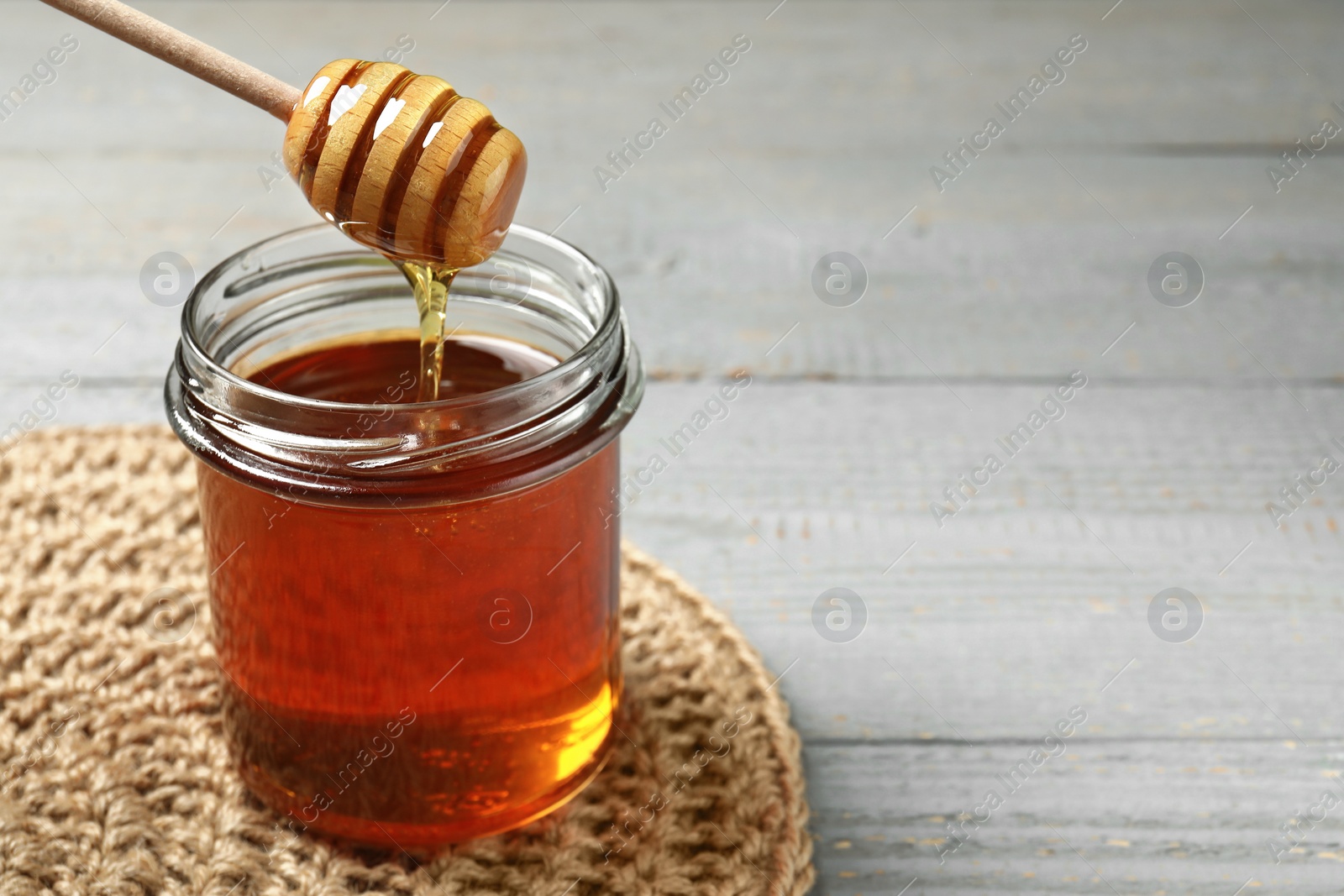 Photo of Pouring tasty honey from dipper into glass jar at grey wooden table, closeup. Space for text