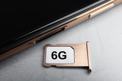 Photo of Internet concept. 6G SIM card in tray and smartphone on light grey table, closeup