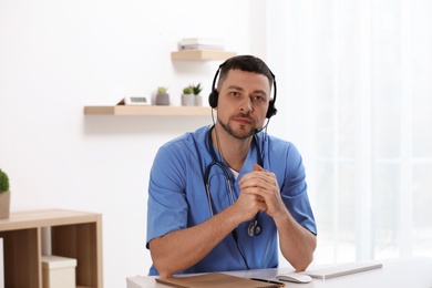 Photo of Doctor with headset sitting at desk in clinic. Health service hotline