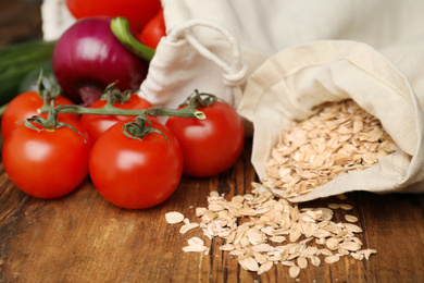 Photo of Cotton eco bags with vegetables and oat flakes on wooden table, closeup