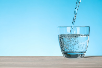 Photo of Pouring water into glass on blue background, space for text. Refreshing drink