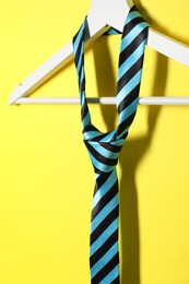 Photo of Hanger with striped necktie on yellow background, closeup