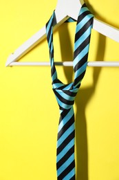 Hanger with striped necktie on yellow background, closeup