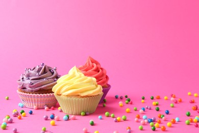 Photo of Delicious cupcakes with bright cream and sprinkles on pink background. Space for text