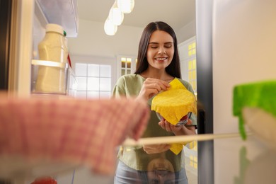 Photo of Happy woman taking away beeswax food wrap, view from refrigerator