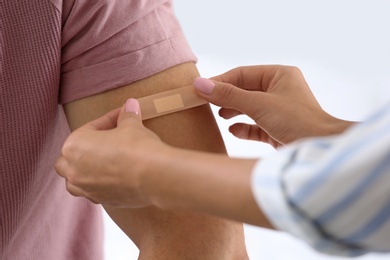 Photo of Woman applying adhesive bandage on man's arm against light background, closeup
