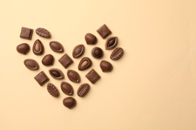 Photo of Heart made with delicious chocolate candies on beige background, top view. Space for text