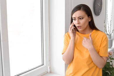 Woman arguing on mobile phone near window at home