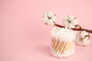 Photo of Container with cotton buds and flowers on pink background. Space for text