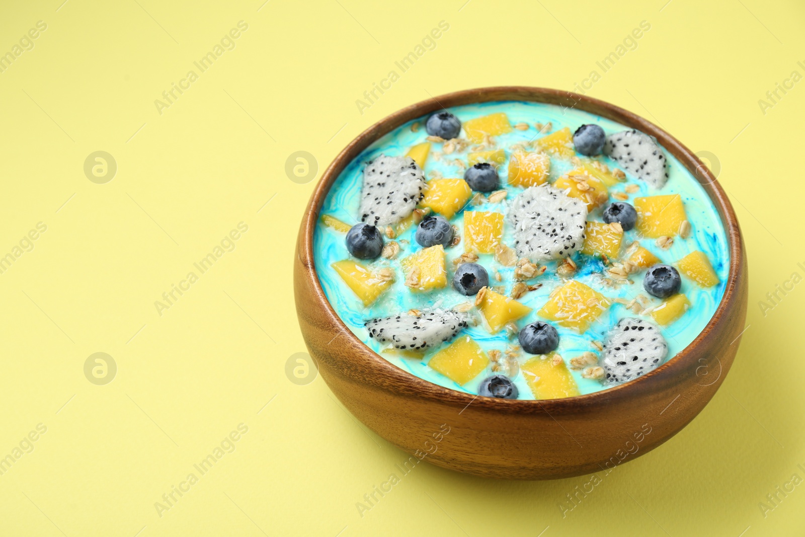 Photo of Delicious smoothie bowl with fresh fruits, blueberries and oatmeal on yellow background. Space for text