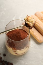 Photo of Tasty tiramisu in glass, coffee beans, spoon and biscuits on light grey table, closeup