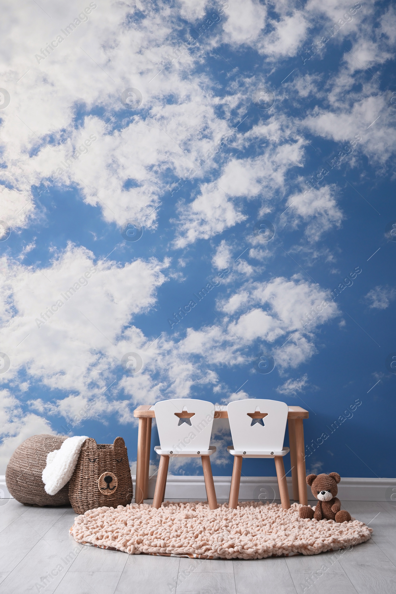 Image of Blue sky with clouds as wallpaper pattern. Baby room interior with table and chairs near wall