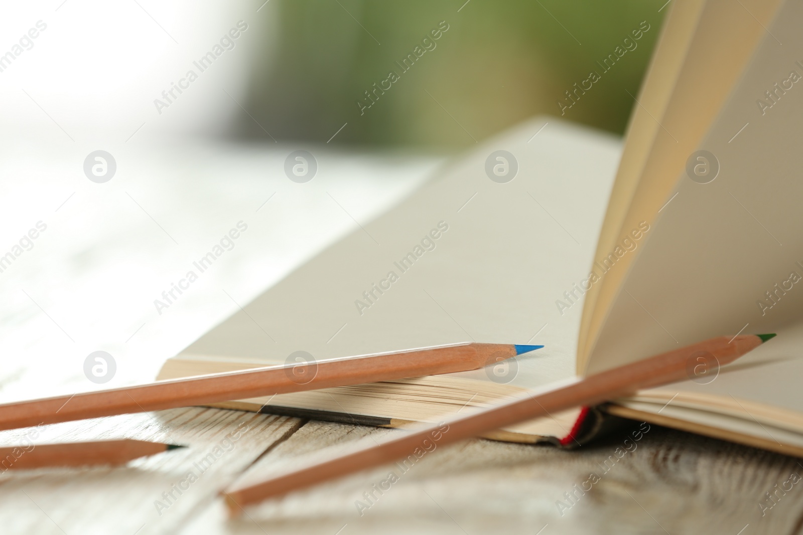 Photo of Closeup view of open notebook with pencils on white wooden table against blurred background