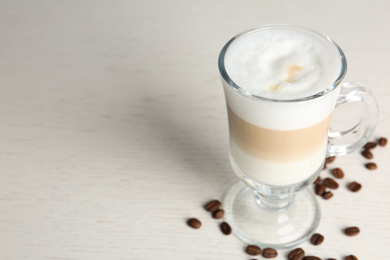 Photo of Delicious latte macchiato and coffee beans on white table, space for text