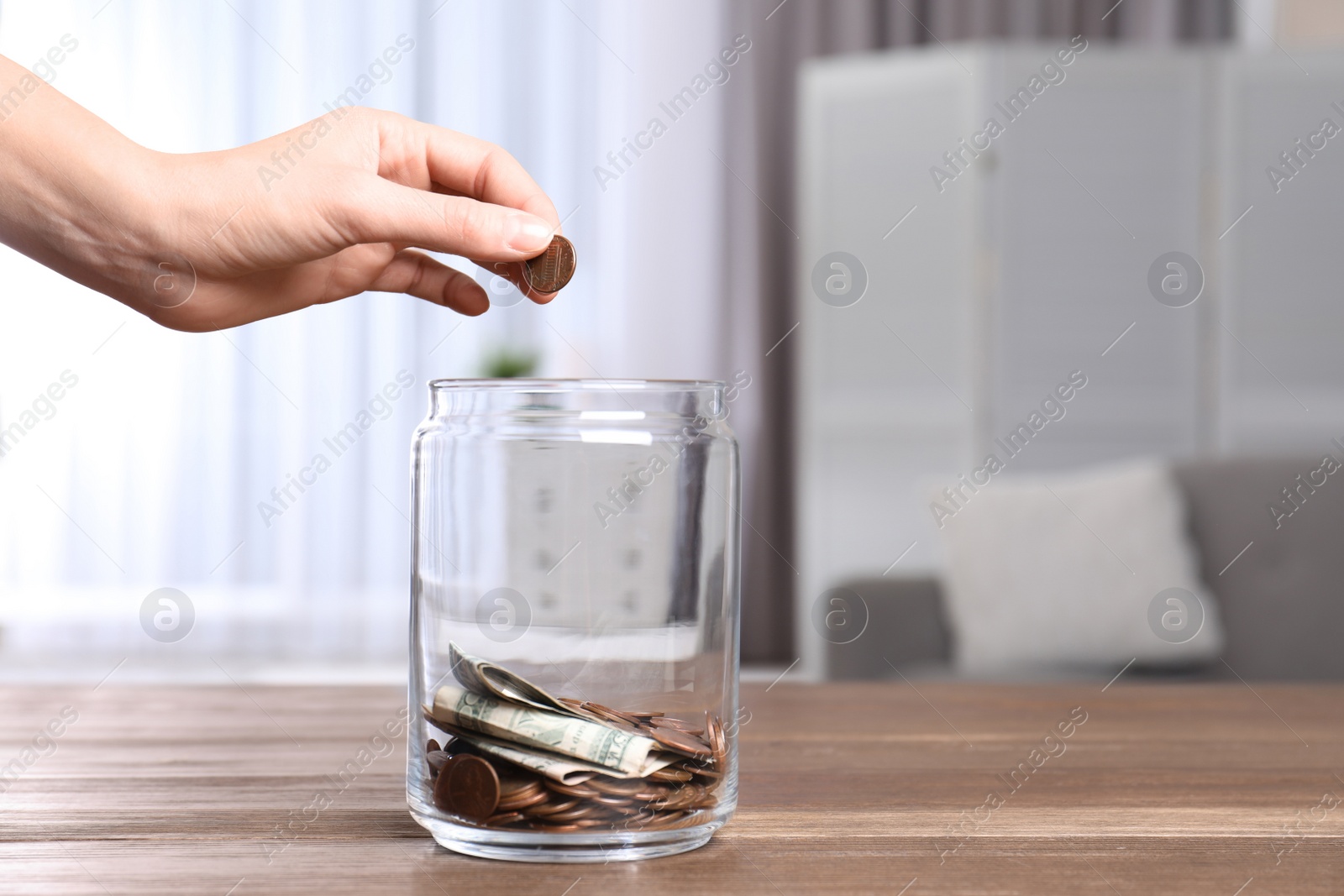 Photo of Woman putting coin into donation jar on table indoors, closeup. Space for text