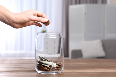 Photo of Woman putting coin into donation jar on table indoors, closeup. Space for text