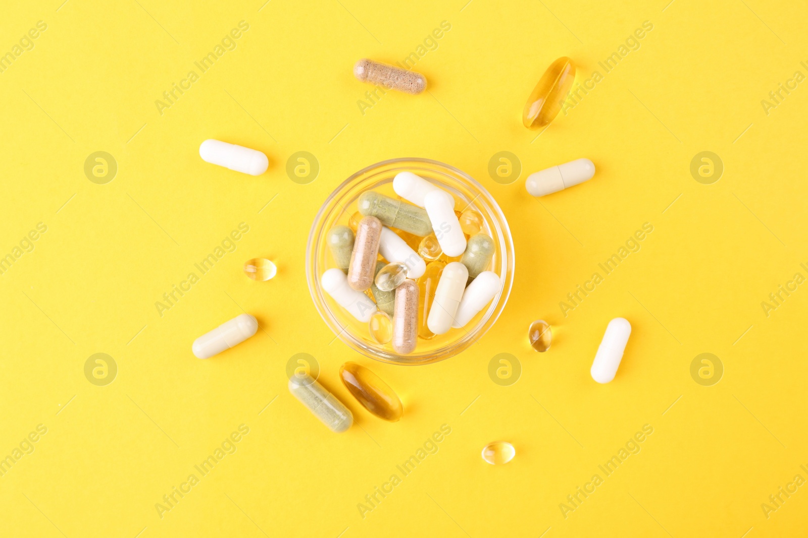 Photo of Different vitamin pills in glass bowl on yellow background, top view