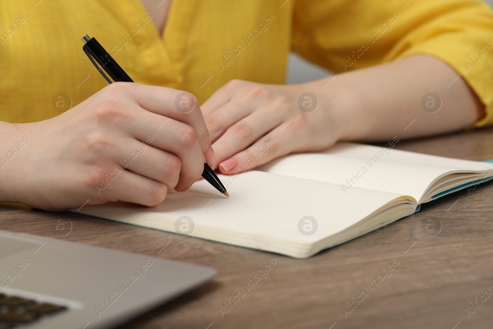 Photo of Woman writing in notebook at wooden table indoors, closeup