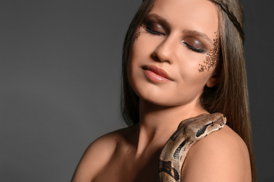 Photo of Beautiful woman with boa constrictor on grey background, closeup