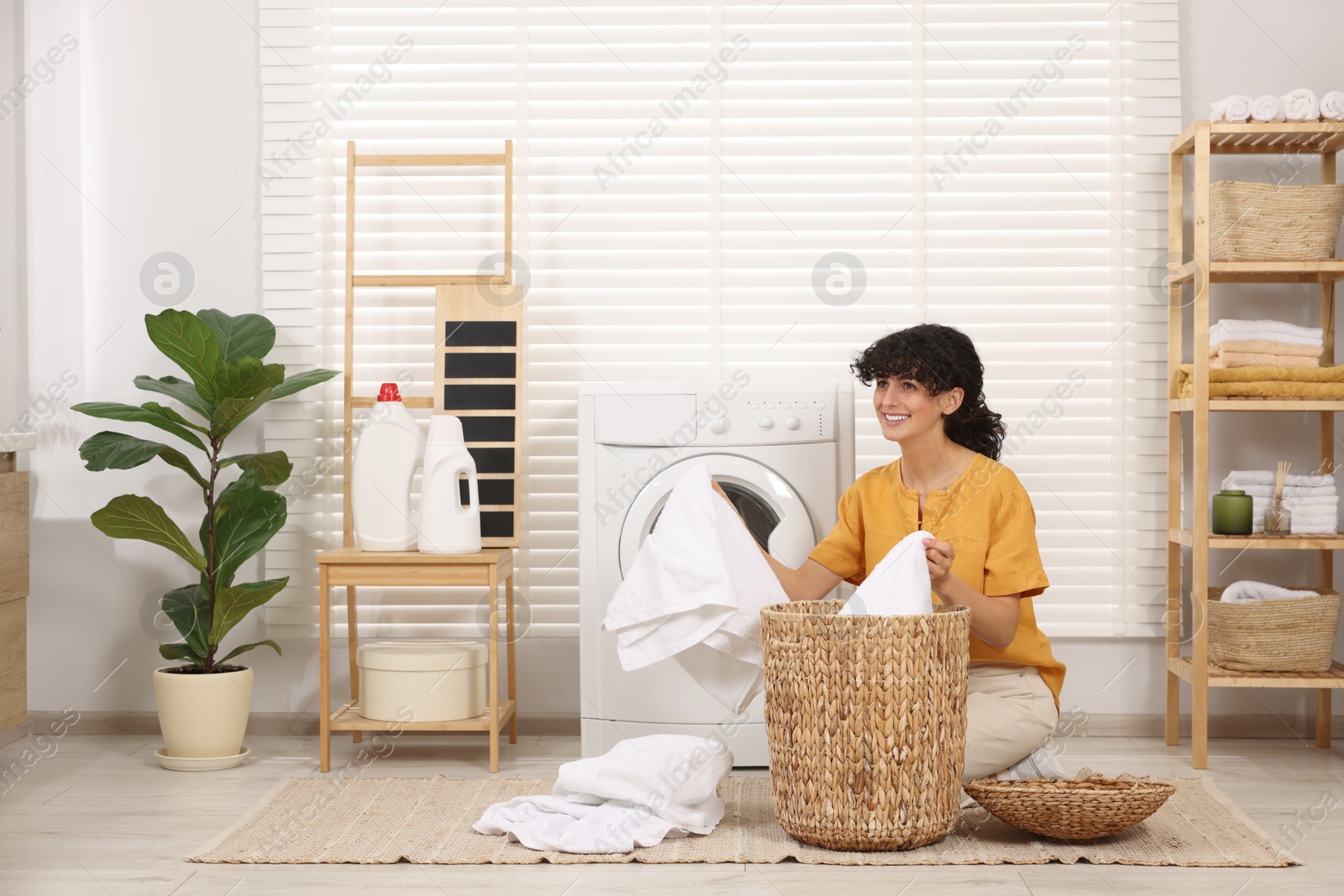 Photo of Happy woman with laundry near washing machine indoors