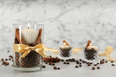 Photo of Glass holders with burning candles, coffee beans and cinnamon on light stone table. Space for text