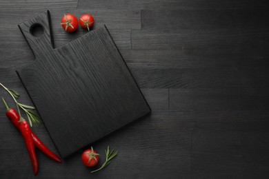 Photo of Cutting board, rosemary, chili peppers and tomatoes on black wooden table, flat lay. Space for text