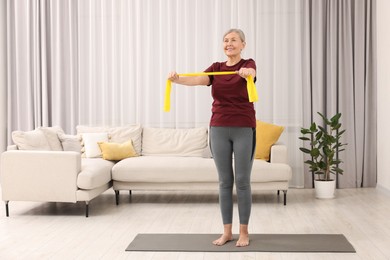 Photo of Senior woman doing exercise with fitness elastic band on mat at home