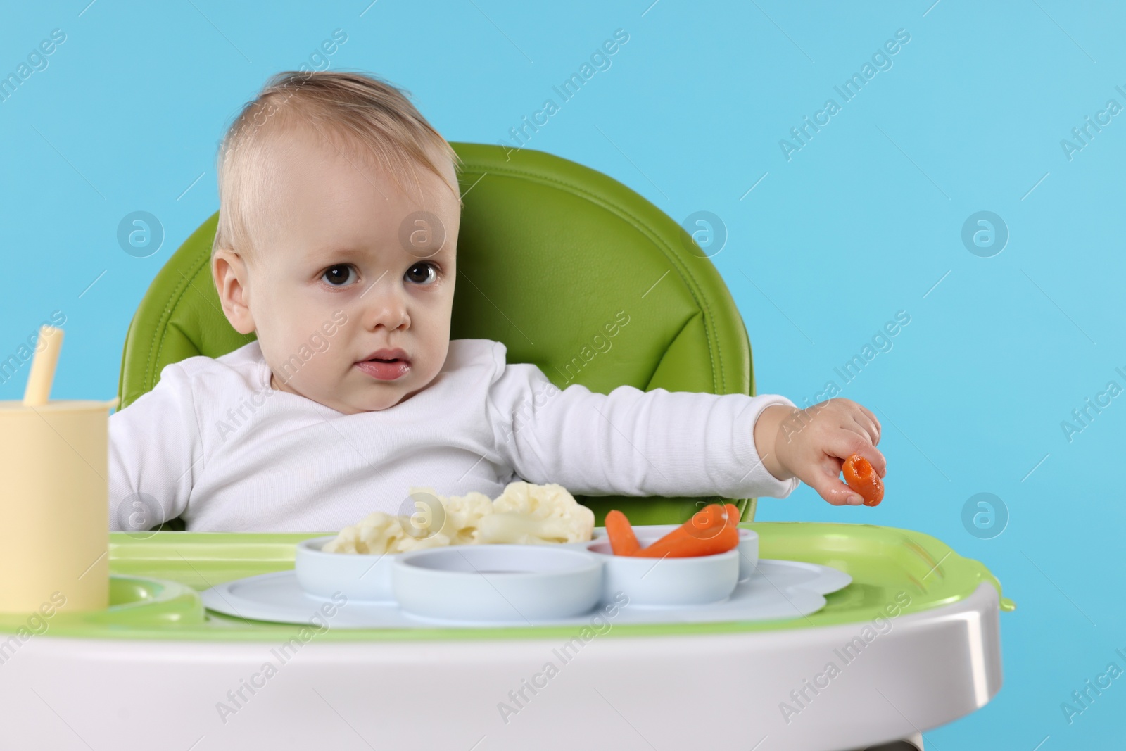 Photo of Cute little baby with healthy food in high chair on light blue background