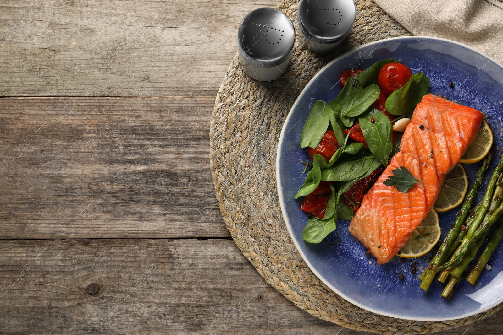 Photo of Tasty grilled salmon with tomatoes, asparagus, spinach and lemon on wooden table, flat lay
