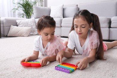 Photo of Little girls playing with pop it fidget toys on floor at home